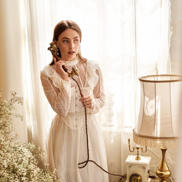 A young woman holds a retro phone, bathed in soft sunlight and delicate decor.